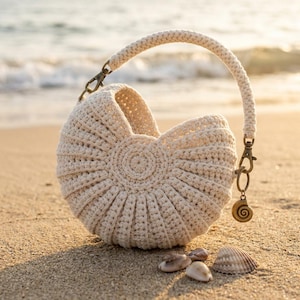 May include: A cream-colored, semi-circular crochet handbag featuring a textured, ribbed pattern and a single arched handle. The bag is accented with antique brass-toned metal hardware, including a small spiral seashell charm attached to the side.