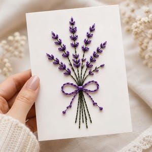 May include: A white rectangular card featuring a hand-embroidered lavender bouquet. The design consists of purple thread flower buds and dark green thread stems, tied together with a purple thread bow at the center of the card.