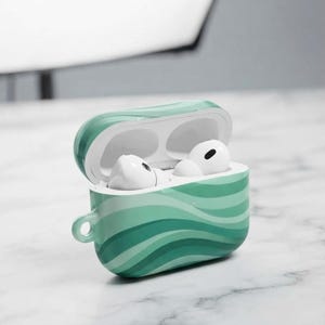May include: A protective case for wireless earbuds featuring a wavy, multi-tonal green pattern. The case is open, revealing two white earbuds nestled inside. A small circular cutout is located on the left side of the case for a lanyard attachment.