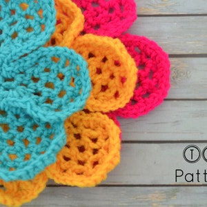 May include: A multi-colored crocheted flower with teal, yellow, and pink petals. The flower is on a wooden surface with the text "TLH Patterns" below it.