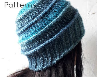 May include: A blue and teal crocheted beanie hat with a slouchy fit. The hat is made with a textured stitch and has a gradient of color from dark blue to teal.