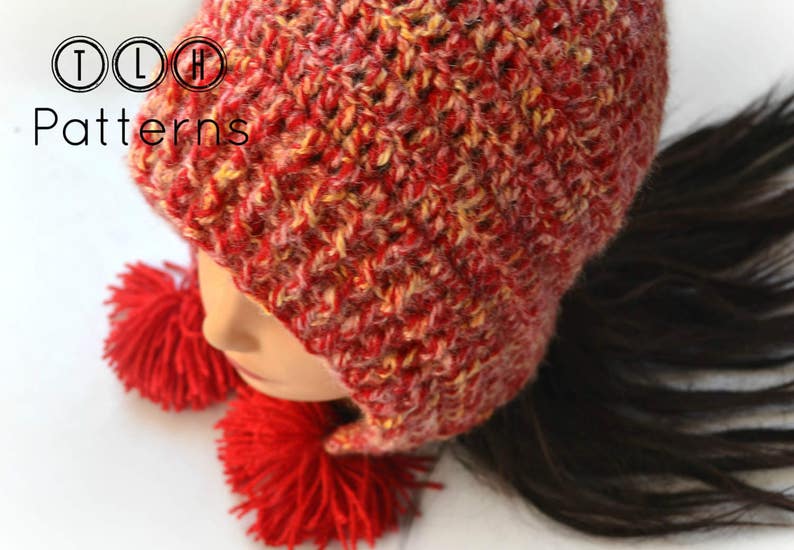 May include: Red and yellow crocheted hat with ear flaps and two red pom-poms. The hat is made with a textured stitch and has a slouchy fit.
