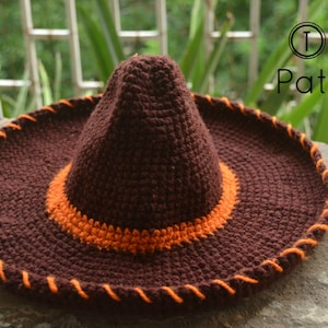 Pode incluir: Um sombrero de croch&ecirc; marrom com uma borda laranja e uma coroa de croch&ecirc; marrom. O chap&eacute;u tem uma borda laranja costurada ao redor da aba.
