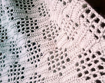 May include: A light gray crocheted shawl with an open, lacy design. The shawl is draped, showcasing the intricate stitch work and texture. The edges have a scalloped pattern. This handmade accessory is suitable for cool weather.