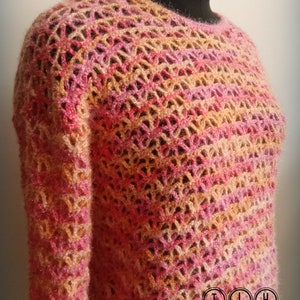 May include: A crocheted sweater with a pink, orange, and beige color pattern. The sweater has a loose, open weave and a round neckline. The sweater is displayed on a mannequin.