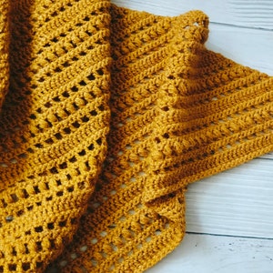 May include: A mustard yellow crocheted shawl with a fringe tassel. The shawl is made with a delicate open stitch pattern.