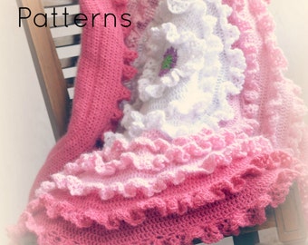 Puede incluir: Una manta de bebé de ganchillo rosa, blanco y rosa claro con un borde de volantes. La manta está drapeada sobre una mecedora de madera. El texto "TLH Patterns" es visible en la esquina superior izquierda de la imagen.
