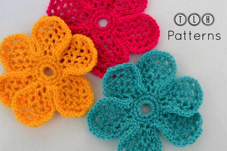 May include: Three crocheted flowers in yellow, pink, and teal. The flowers are all the same design, but in different colors. The flowers are on a white background. TLH Patterns is written in black text on the right side of the image.