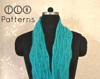 May include: A teal blue crocheted infinity scarf with a textured pattern. The scarf is displayed on a black mannequin.
