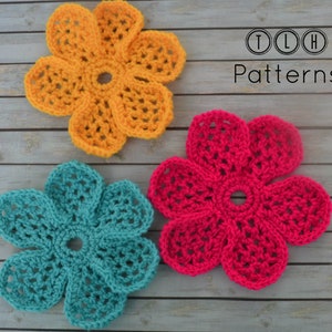 May include: Three crocheted flowers on a wooden background. The flowers are yellow, teal, and pink. The text "TLH Patterns" is in the upper right corner of the image.