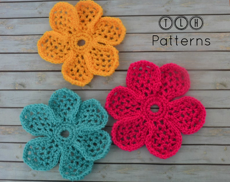 May include: Three crocheted flowers on a wooden background. The flowers are yellow, teal, and pink. The text "TLH Patterns" is in the upper right corner of the image.