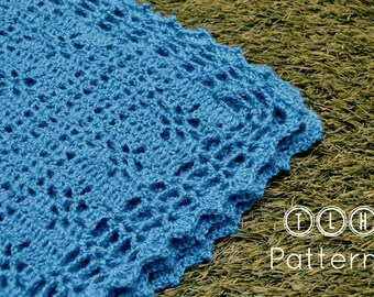 Puede incluir: Primer plano de una manta de ganchillo azul con un patrón de encaje. La manta está doblada y el borde es visible. La manta está sobre un fondo verde.