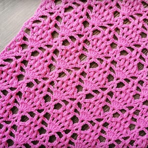 May include: A close-up of a handmade, pink crochet item. The crochet pattern has a repeating floral design with openwork details. The texture is soft and the colour is a vibrant, medium pink.