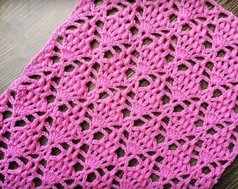 May include: A close-up shot of a handmade, pink crochet piece. The crochet pattern features a repeating floral design with openwork details. The texture is soft and the color is a vibrant, medium pink.