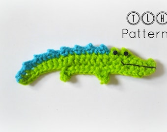 Puede incluir: Un cocodrilo de crochet verde y azul con ojos negros. El cocodrilo está sobre un fondo blanco.