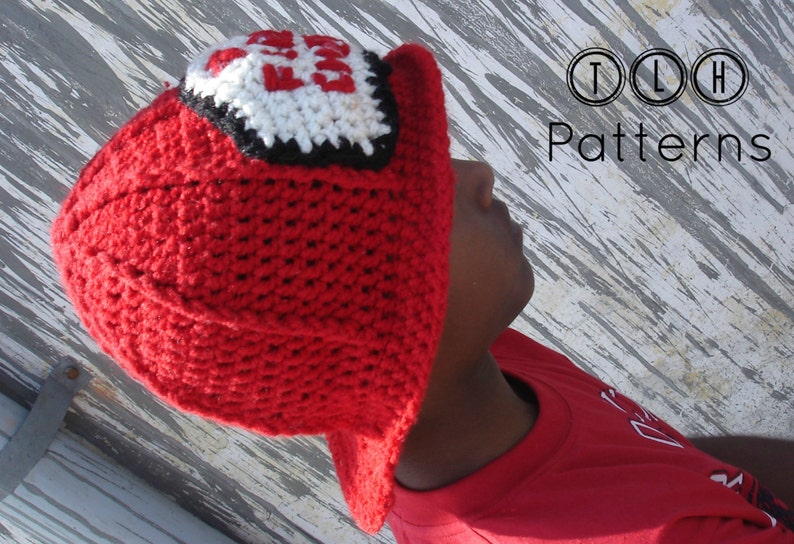 May include: A red crocheted hat with a white and black patch that says "Fire Chief" on it. The hat is being worn by a person with a red shirt.