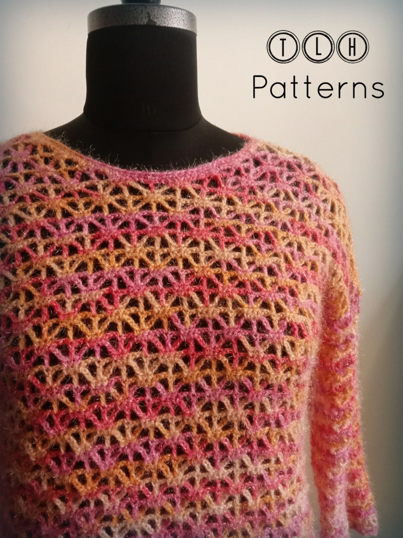 May include: A crocheted sweater in shades of pink, orange, and brown. The sweater has a lacy pattern and is displayed on a mannequin.