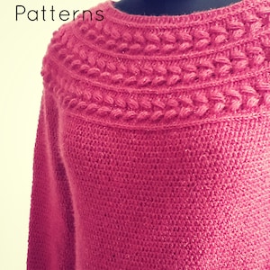 Könnte beinhalten: Ein rosa gestrickter Pullover mit einem Zopfmuster um den Halsausschnitt. Der Pullover ist aus weichem, flauschigem Garn gefertigt.