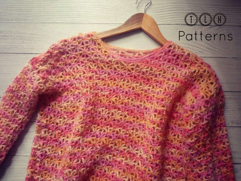 May include: A crocheted sweater in a pink, orange, and white color scheme. The sweater has a loose, open-weave design and a round neckline.