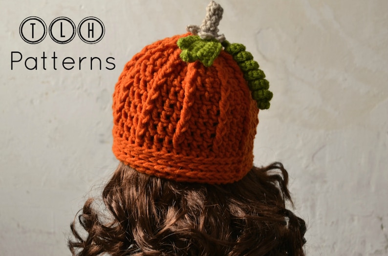 May include: A crocheted pumpkin hat in orange with a green stem and leaves. The hat is worn on a person with brown curly hair. The text "TLH Patterns" is visible in the top left corner of the image.