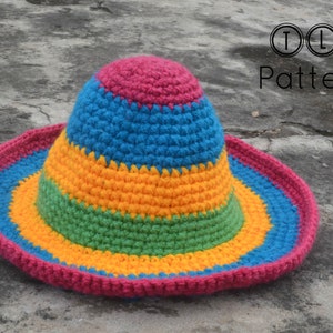 Pode incluir: Um chap&eacute;u de sol de croch&ecirc; colorido com listras rosa, azul, amarelo e verde. O chap&eacute;u est&aacute; sobre uma superf&iacute;cie de concreto cinza.