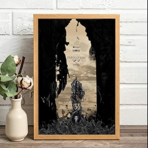Puede incluir: Un póster vertical enmarcado que muestra una entrada de caverna oscura y dentada con un monolito de piedra central marcado con el número 33. El texto dice Kepler, Sandfall Interactive y Expedition 33. El marco es de madera clara.