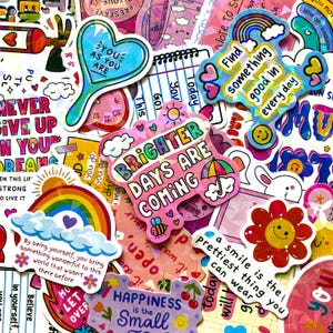 Può includere: Una collezione di adesivi in vinile colorati con varie citazioni motivazionali e illustrazioni tra cui arcobaleni, fiori, cuori e nuvole. I design incorporano testi come Brighter days are coming, Find something good in everyday e You as you are.