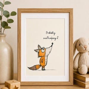 Puede incluir: Una lámina de arte enmarcada con una ilustración dibujada a mano de un zorro naranja y blanco mirando hacia arriba con ojos grandes. El texto "Probably overthinking it." está escrito en negro sobre el zorro. El marco es de madera clara.