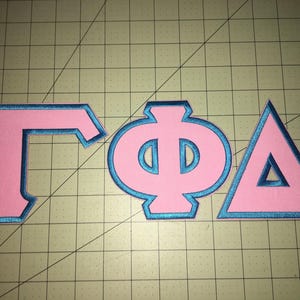May include: Three Greek letters, Gamma, Phi, and Delta, are outlined in teal blue and filled in with pink. The letters are arranged from left to right.