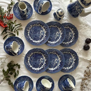 May include: A blue and white ceramic tea set featuring a detailed landscape pattern. The collection includes a teapot, a lidded sugar bowl, a creamer, six teacups with matching saucers, and six plates, all decorated with intricate floral and scenery motifs.