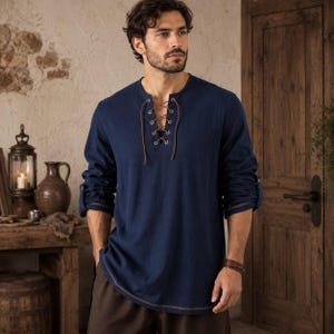 May include: A long-sleeved navy blue shirt featuring a lace-up front closure with brown cord threaded through metal grommets. The shirt has a rounded neckline, a straight hemline with visible brown stitching, and sleeves that are rolled up to the elbows.