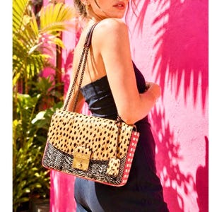 May include: A rectangular shoulder bag featuring a top flap with a tan and black leopard print pattern. The lower section displays a black and white chevron design. It includes a gold-tone metal clasp, a chain strap, and a small matching charm.