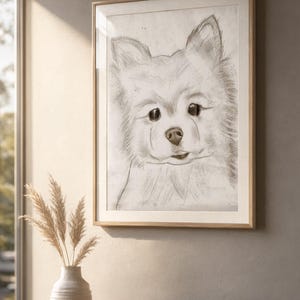 Könnte beinhalten: Eine gerahmte Kohlezeichnung eines flauschigen Hundes mit spitzen Ohren und dunklen Augen. Das Kunstwerk ist in Grau- und Schwarztönen auf weißem Hintergrund gehalten und befindet sich in einem hellen Holzrahmen mit schlichtem Design.