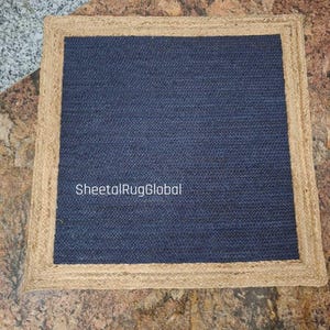 May include: A square rug featuring a dark blue woven center panel surrounded by a wide, natural tan jute border. The text SheetalRugGlobal is printed in white across the center of the blue section of this flat-woven floor covering.