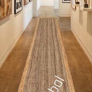 May include: A long, rectangular runner rug featuring a textured, woven surface in shades of beige and light brown with a distinct border. The rug is positioned centrally on a smooth floor in a hallway. The text SheetalRugGlobal is visible.