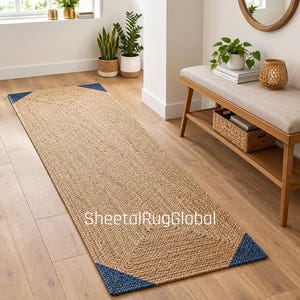 May include: A rectangular runner rug made of natural tan woven jute fibers with dark blue triangular accents at each of the four corners. The rug features a textured, braided surface pattern and includes the text SheetalRugGlobal printed on it.