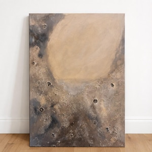 Puede incluir: Un cuadro rectangular sobre lienzo que presenta una gran forma circular beige y lisa sobre un fondo texturizado de color marrón oscuro y gris. La parte inferior de la obra muestra capas de empaste grueso con pequeñas hendiduras circulares oscuras.
