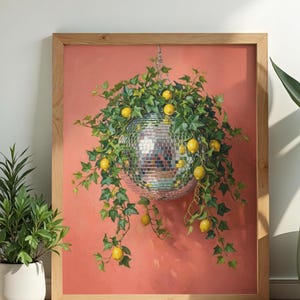 May include: A framed wall art print featuring a silver mirrored disco ball hanging from a chain, surrounded by lush green ivy vines and bright yellow lemons, all set against a solid coral-colored background within a light wood frame.