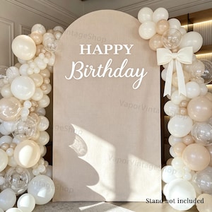 Peut inclure: Une toile de fond arquée beige avec le texte blanc HAPPY Birthday, décorée d'une guirlande de ballons denses dans des tons crème, beige et transparent, agrémentée d'un grand nœud en tissu crème sur le côté droit. Support non inclus.