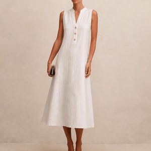 May include: A sleeveless white midi dress featuring a mandarin collar, a V-neckline, and a front placket with three light brown buttons. The dress has a straight, relaxed silhouette that falls to the mid-calf, crafted from a textured fabric.