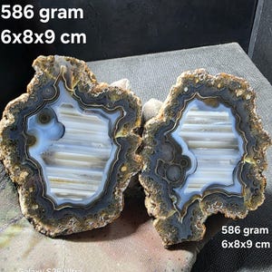 以下が含まれることがあります： 青、白、茶色の鉱物堆積物の同心円状の帯が特徴のメノウのジオードスライス2枚。重さは586グラム、サイズは6x8x9cm。内部には水平な白い結晶層が見られ、周囲は暗く質感のある縁で囲まれています。