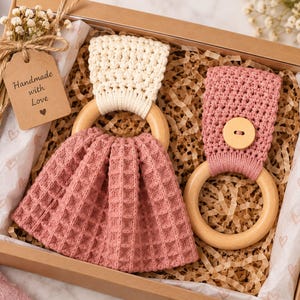 May include: A gift box containing two wooden ring towel holders. One features a cream-coloured crocheted top with a dusty rose waffle-weave fabric. The other has a dusty rose crocheted top with a wooden button. A tag reads Handmade with Love.