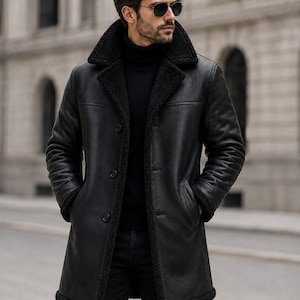 May include: A black leather coat featuring a wide lapel collar lined with black faux shearling, long sleeves with matching cuffs, a three-button front closure, and two side pockets, worn over a black turtleneck jumper and black trousers.