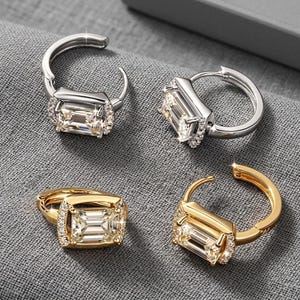 May include: Two pairs of hoop earrings featuring emerald-cut clear stones surrounded by small pavé accents. One pair is finished in a polished silver tone, while the other pair is finished in a polished gold tone, both with hinged closures.