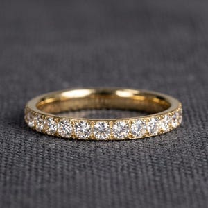 Op de afbeelding: Een gouden eternity ring met een doorlopende rij kleine, ronde, helder gefacetteerde stenen die langs de gehele buitenomtrek van de gepolijste geelgouden band zijn gezet, wat een uniform en sprankelend cirkelvormig sieraad creëert.