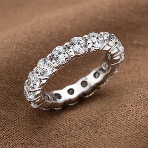 Op de afbeelding: Een zilverkleurige eternity ring met een doorlopende rij ronde, heldere, gefacetteerde stenen in een gepolijste metalen zetting. De ring toont een gelijkmatige rangschikking van fonkelende stenen die rondom de gehele omtrek zijn geplaatst.