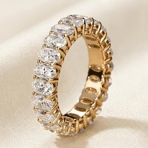 Peut inclure: Une alliance en or ornée d'une rangée continue de pierres claires taille ovale fixées par des griffes. La bague présente une finition métallique polie et un agencement uniforme de gemmes facettées qui entourent toute la circonférence.