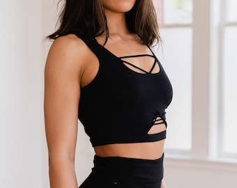 May include: A woman wearing a black crop top with criss-cross straps and black shorts with cutouts on the sides. The shorts have a high waist and are made of a stretchy material.
