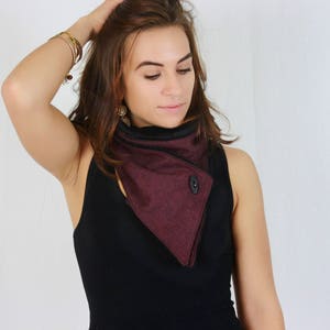 May include: A woman wearing a black sleeveless top with a burgundy and black cowl neck scarf. The scarf has a button closure.