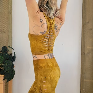 May include: A mustard yellow crop top and leggings set with a unique cut-out design on the back of the top and down the sides of the leggings.
